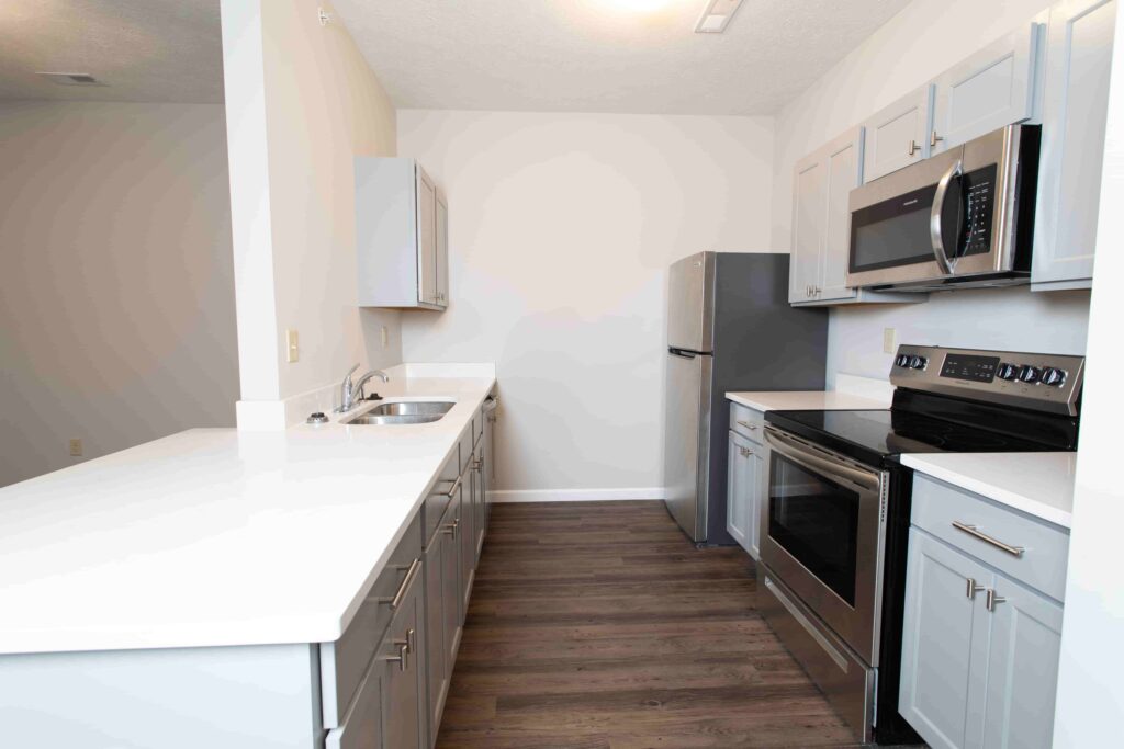 Modern galley kitchen with white countertops, stainless steel appliances, gray cabinets, and dark wood flooring.